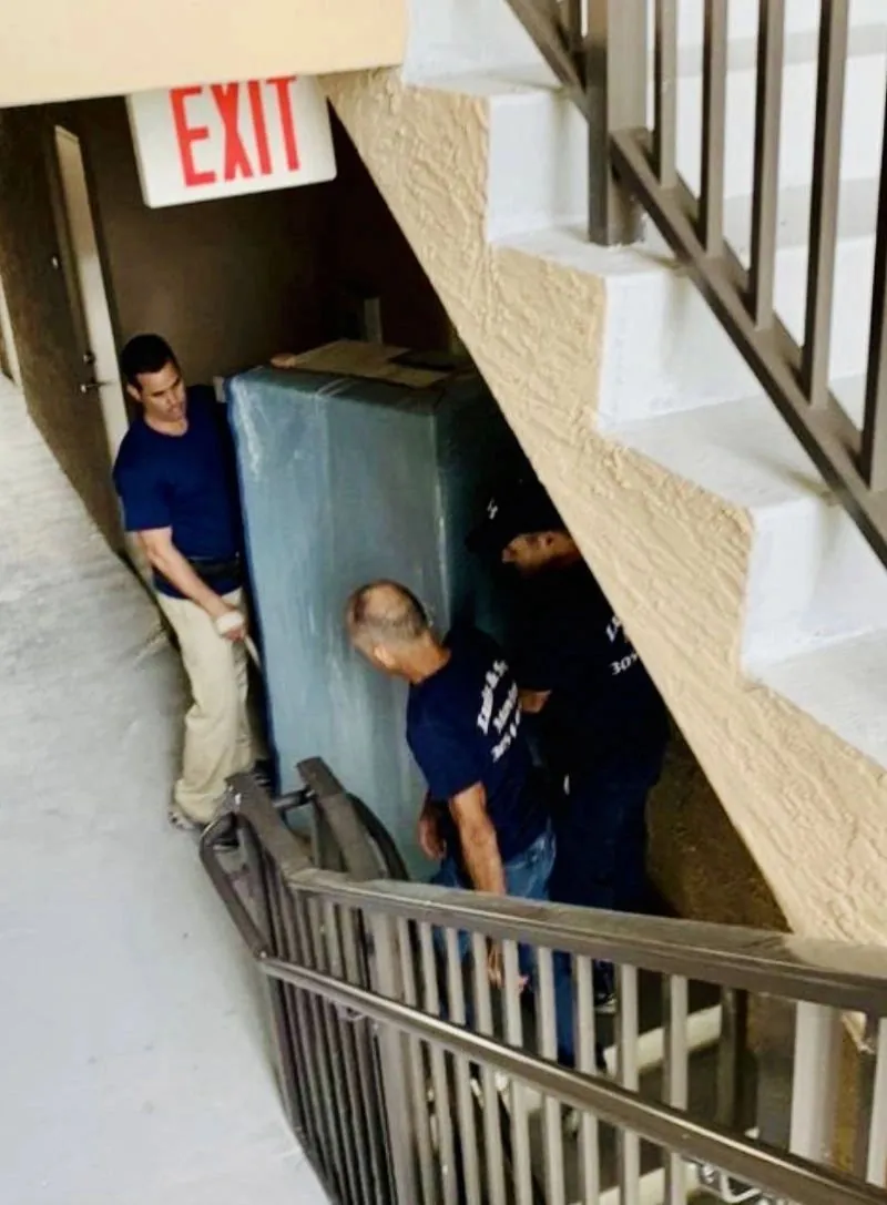Luis & Son movers carrying a wrapped piece of furniture down a stairwell