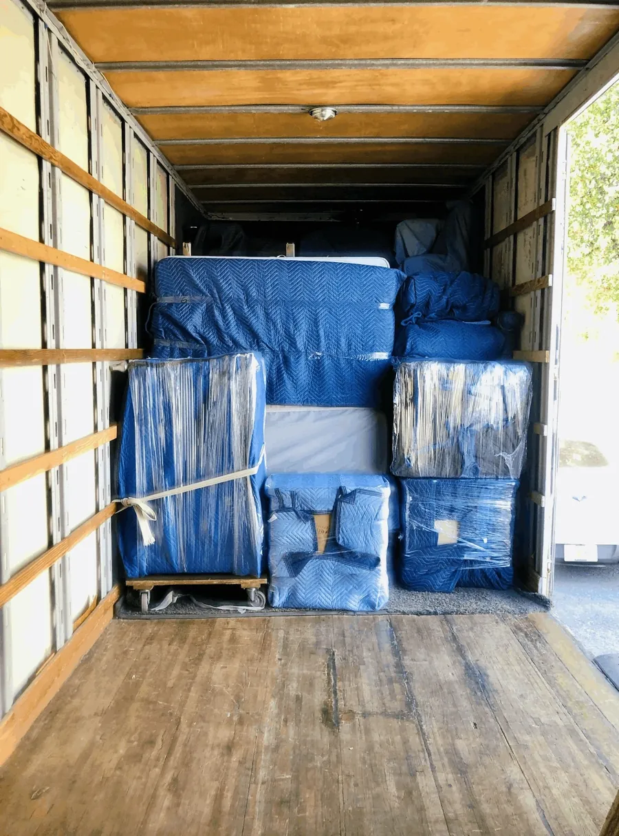 Furniture wrapped in blue moving blankets and strapped inside the truck