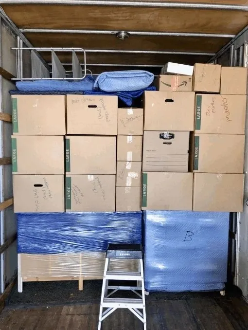 Labeled boxes stacked floor to ceiling over wrapped furniture